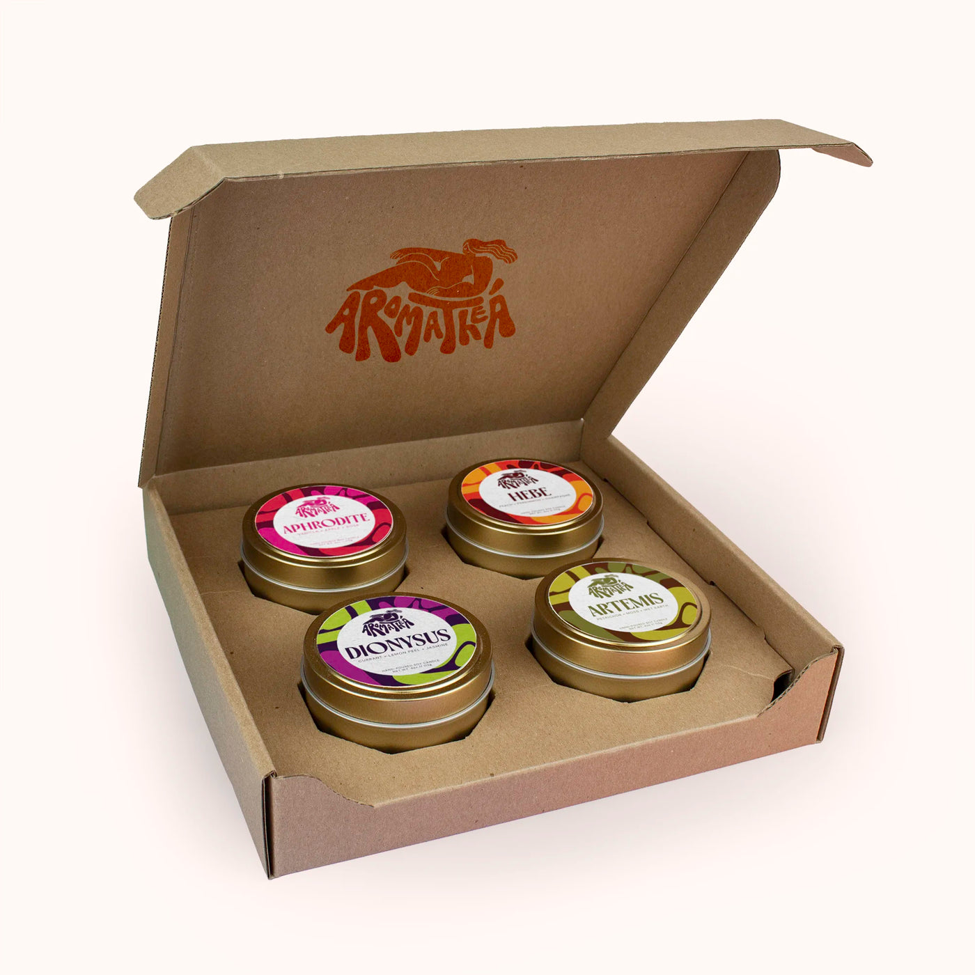 Four candle tins with decorative labels in a cardboard box featuring a brand logo and the words 'Aromatheá'